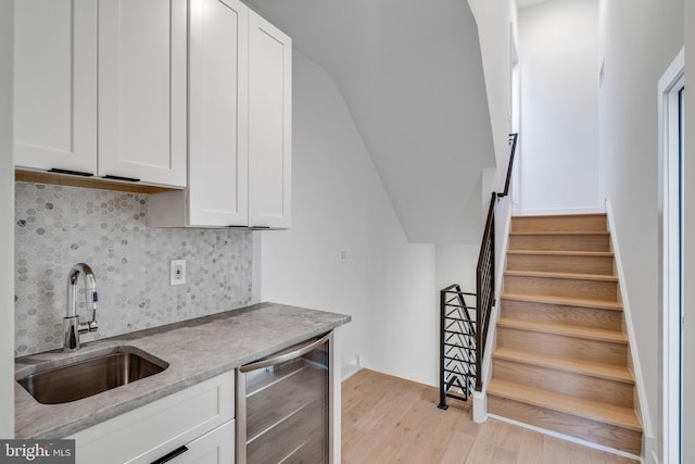 bar with wine cooler, sink, white cabinetry, light hardwood / wood-style floors, and decorative backsplash