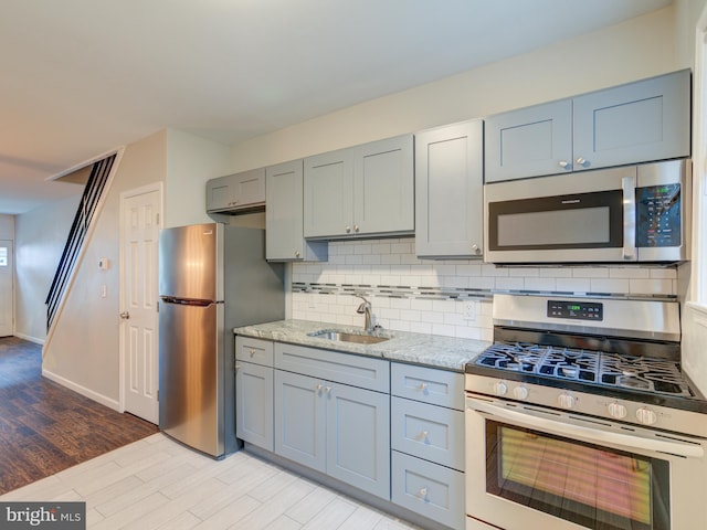 kitchen featuring light stone counters, backsplash, appliances with stainless steel finishes, light hardwood / wood-style flooring, and sink