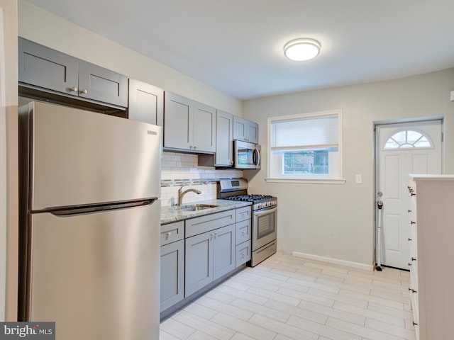 kitchen with appliances with stainless steel finishes, a healthy amount of sunlight, sink, and light stone counters