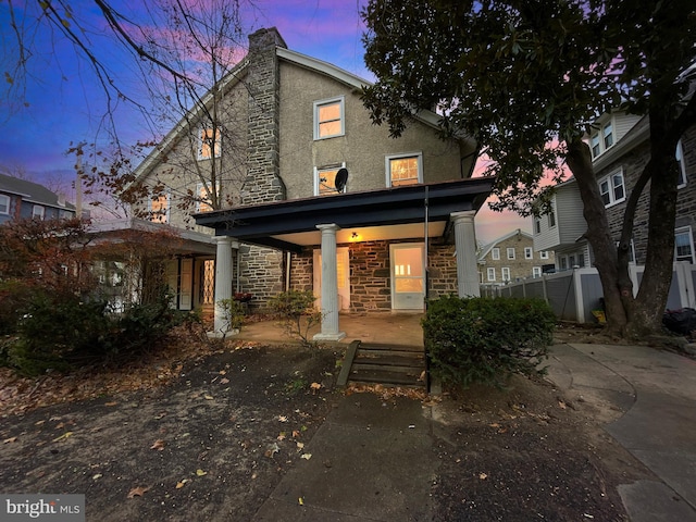 back house at dusk featuring covered porch