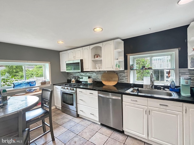 kitchen with light tile patterned flooring, sink, white cabinetry, stainless steel appliances, and backsplash