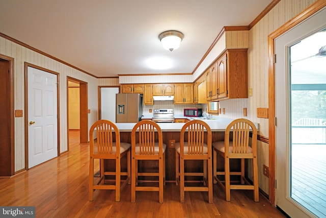 kitchen featuring ornamental molding, stainless steel appliances, a breakfast bar area, and light hardwood / wood-style flooring