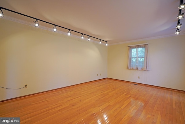 empty room with ornamental molding, light hardwood / wood-style floors, and rail lighting