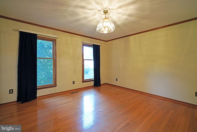 empty room featuring hardwood / wood-style flooring, an inviting chandelier, and ornamental molding