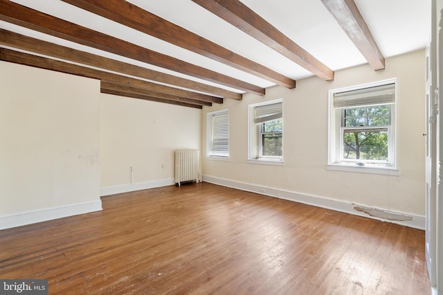 spare room with radiator heating unit, beamed ceiling, and wood-type flooring