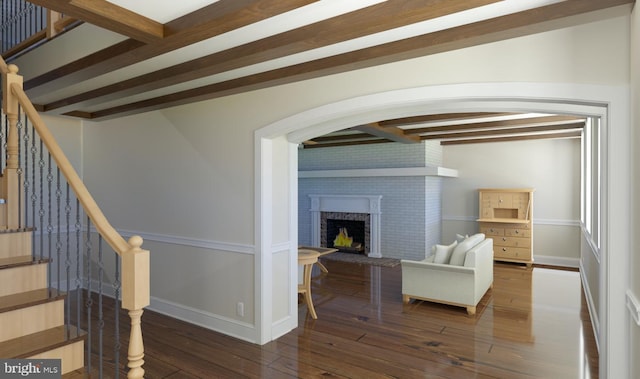 living room featuring beamed ceiling, a brick fireplace, and dark hardwood / wood-style flooring