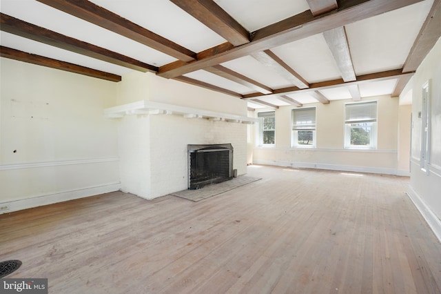 unfurnished living room featuring a brick fireplace, beamed ceiling, and light wood-type flooring