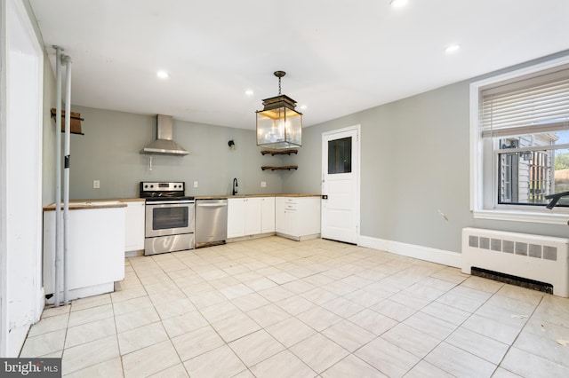 kitchen with wall chimney exhaust hood, hanging light fixtures, radiator heating unit, stainless steel appliances, and white cabinets