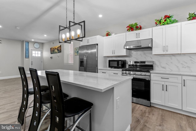 kitchen featuring white cabinetry, light stone counters, stainless steel appliances, and a kitchen breakfast bar