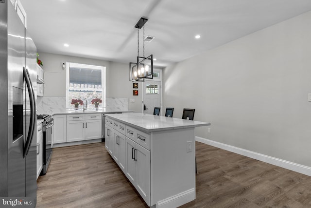 kitchen featuring white cabinetry, hanging light fixtures, appliances with stainless steel finishes, dark hardwood / wood-style floors, and a kitchen island