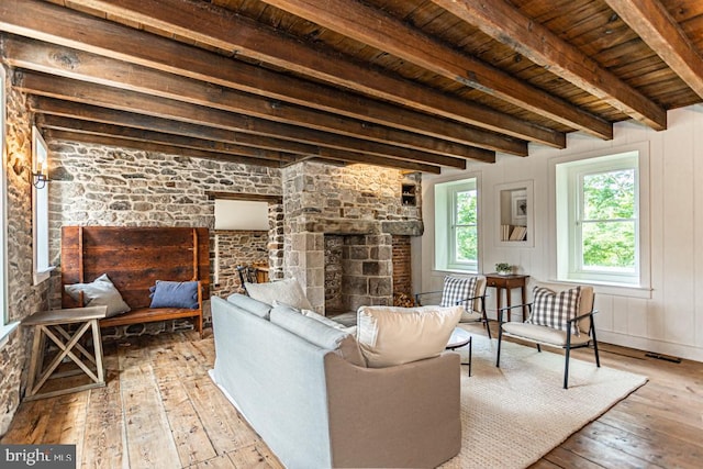 living room with wooden ceiling, beam ceiling, a stone fireplace, and light wood-type flooring