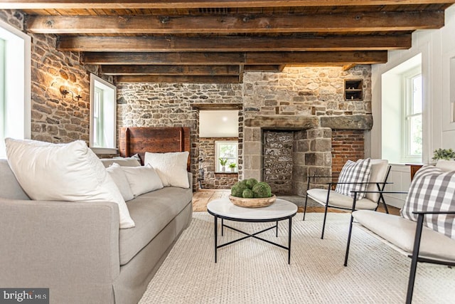 living room with a stone fireplace and beamed ceiling