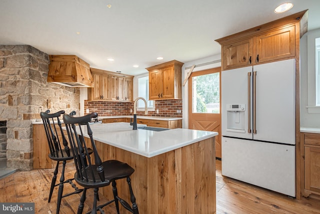 kitchen with premium range hood, high end white refrigerator, sink, a kitchen bar, and light hardwood / wood-style floors