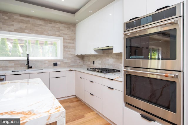 kitchen with backsplash, sink, appliances with stainless steel finishes, light stone counters, and light hardwood / wood-style floors