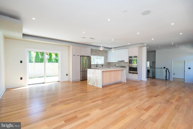 kitchen featuring backsplash, light hardwood / wood-style floors, a kitchen island, stainless steel appliances, and white cabinets