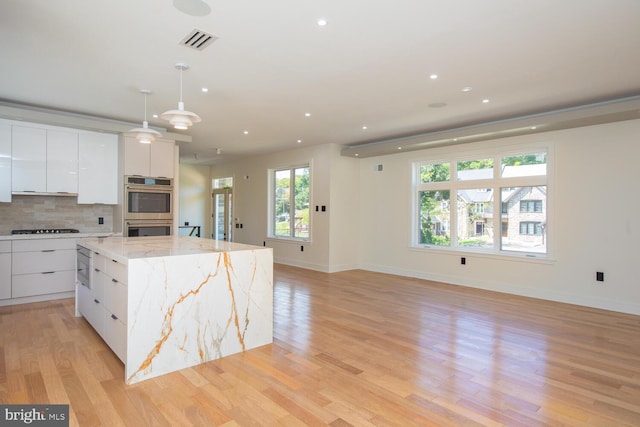 kitchen with decorative backsplash, light hardwood / wood-style flooring, white cabinetry, light stone countertops, and double oven