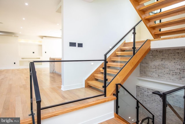 stairway featuring wood-type flooring and brick wall