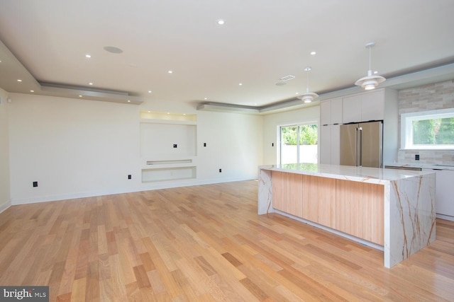 kitchen with light wood-type flooring, decorative backsplash, high quality fridge, a kitchen island, and white cabinetry