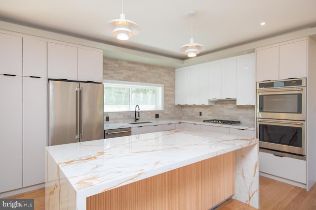 kitchen with light wood-type flooring, appliances with stainless steel finishes, light stone counters, and white cabinetry