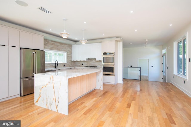 kitchen featuring light wood-type flooring, tasteful backsplash, appliances with stainless steel finishes, light stone counters, and a center island