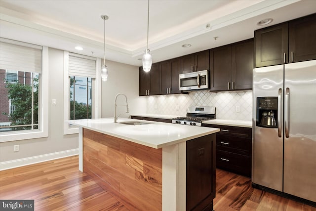 kitchen with dark brown cabinetry, appliances with stainless steel finishes, dark hardwood / wood-style flooring, tasteful backsplash, and a kitchen island with sink