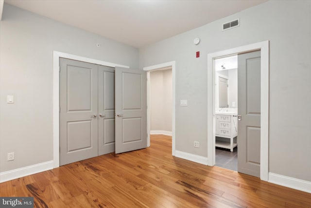 unfurnished bedroom with hardwood / wood-style flooring, a closet, and ensuite bath