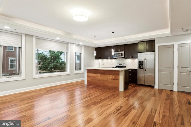 kitchen featuring pendant lighting, a tray ceiling, stainless steel appliances, and an island with sink