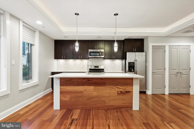 kitchen with wood-type flooring, hanging light fixtures, backsplash, stainless steel appliances, and dark brown cabinetry