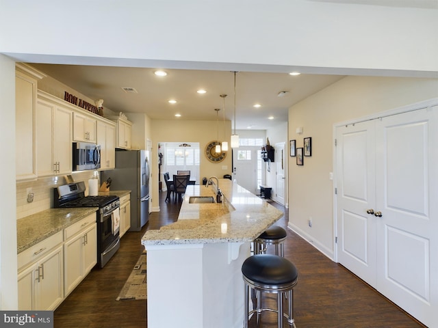 kitchen featuring appliances with stainless steel finishes, decorative light fixtures, dark hardwood / wood-style floors, light stone countertops, and a kitchen breakfast bar