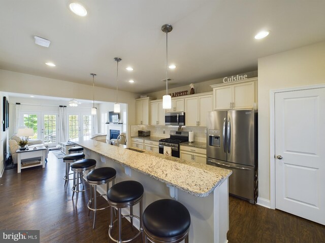 kitchen with decorative backsplash, dark wood-type flooring, a spacious island, a kitchen bar, and stainless steel appliances