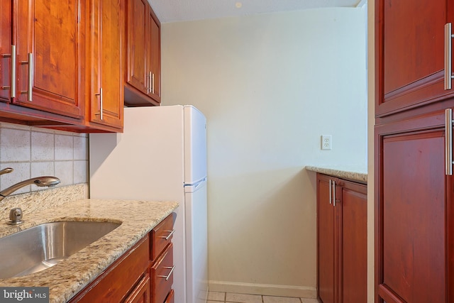 kitchen featuring light tile patterned flooring, sink, backsplash, white fridge, and light stone counters