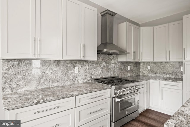 kitchen featuring wall chimney exhaust hood, white cabinetry, light stone counters, stainless steel range, and decorative backsplash