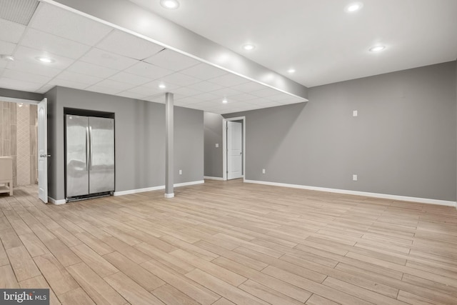 basement with light hardwood / wood-style floors and stainless steel refrigerator