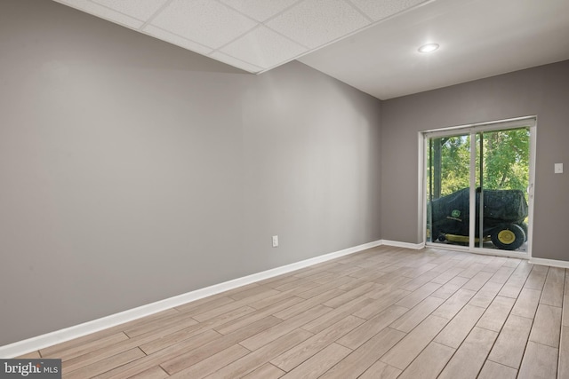 empty room with a drop ceiling and light hardwood / wood-style floors