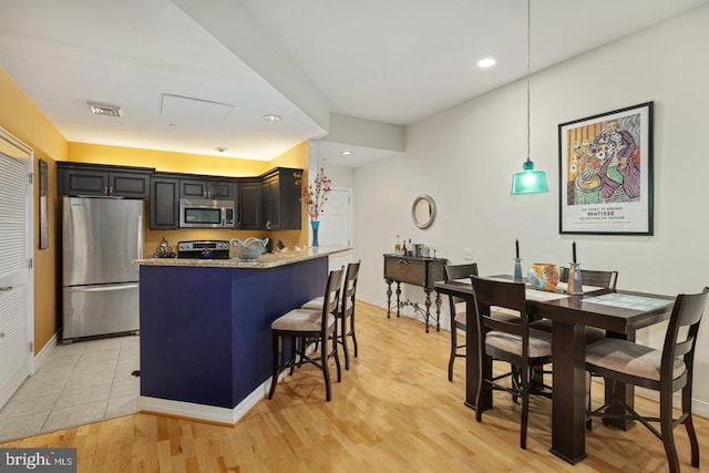 kitchen featuring light hardwood / wood-style flooring, pendant lighting, light stone countertops, stainless steel appliances, and a breakfast bar