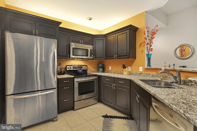 kitchen with light stone counters, appliances with stainless steel finishes, dark brown cabinets, light tile patterned floors, and sink