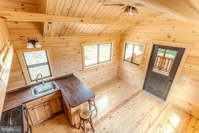 interior space featuring vaulted ceiling with beams, wood walls, a sink, and light wood-style floors