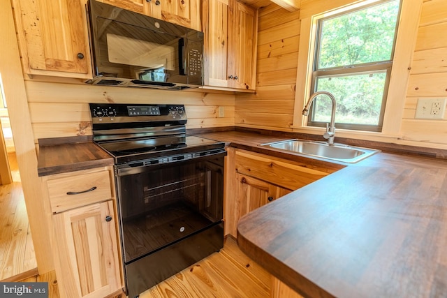 kitchen featuring black appliances, wood walls, dark countertops, and a sink