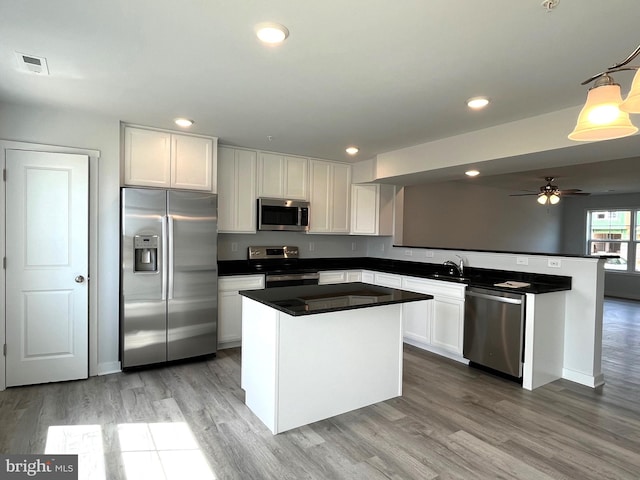 kitchen with appliances with stainless steel finishes, a center island, white cabinets, and light hardwood / wood-style flooring