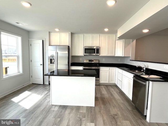 kitchen with a kitchen island, appliances with stainless steel finishes, white cabinetry, sink, and light wood-type flooring