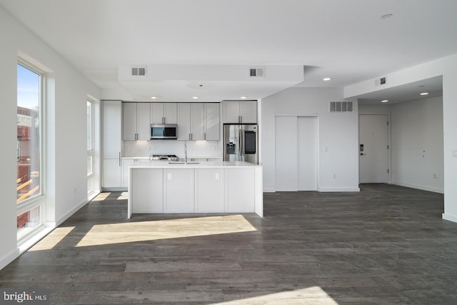 kitchen with appliances with stainless steel finishes, dark hardwood / wood-style floors, backsplash, and an island with sink