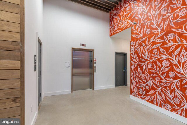 corridor featuring elevator, a towering ceiling, and beam ceiling