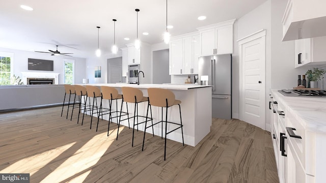 kitchen featuring a kitchen island with sink, white cabinetry, appliances with stainless steel finishes, decorative light fixtures, and light hardwood / wood-style flooring