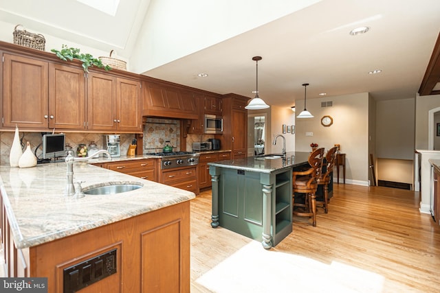 kitchen with pendant lighting, sink, stainless steel appliances, light stone countertops, and a large island with sink