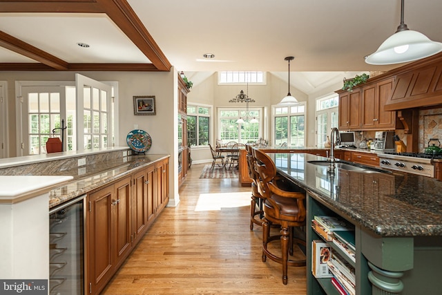 kitchen featuring a center island with sink, beverage cooler, hanging light fixtures, and dark stone countertops