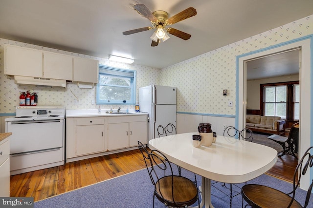 kitchen featuring sink, white appliances, hardwood / wood-style floors, a healthy amount of sunlight, and white cabinets