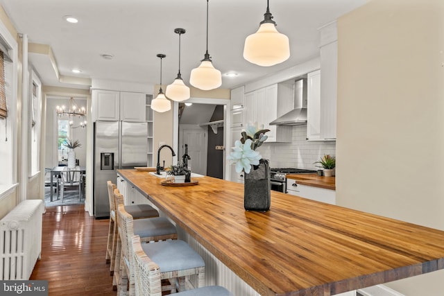 kitchen featuring white cabinetry, butcher block counters, and wall chimney exhaust hood