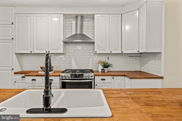 kitchen with wooden counters, wall chimney range hood, gas stove, and white cabinets