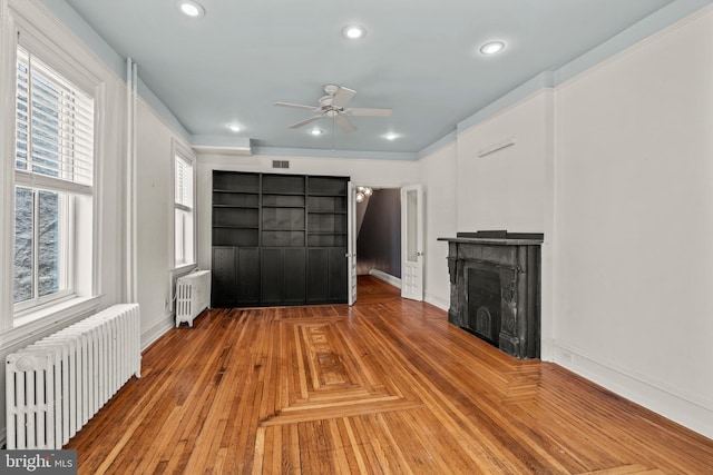 unfurnished living room featuring a wealth of natural light, radiator, and wood-type flooring