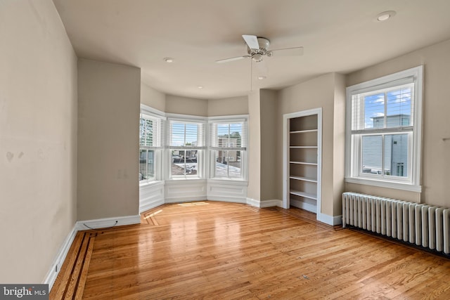 unfurnished room featuring light wood-type flooring, plenty of natural light, ceiling fan, and radiator heating unit